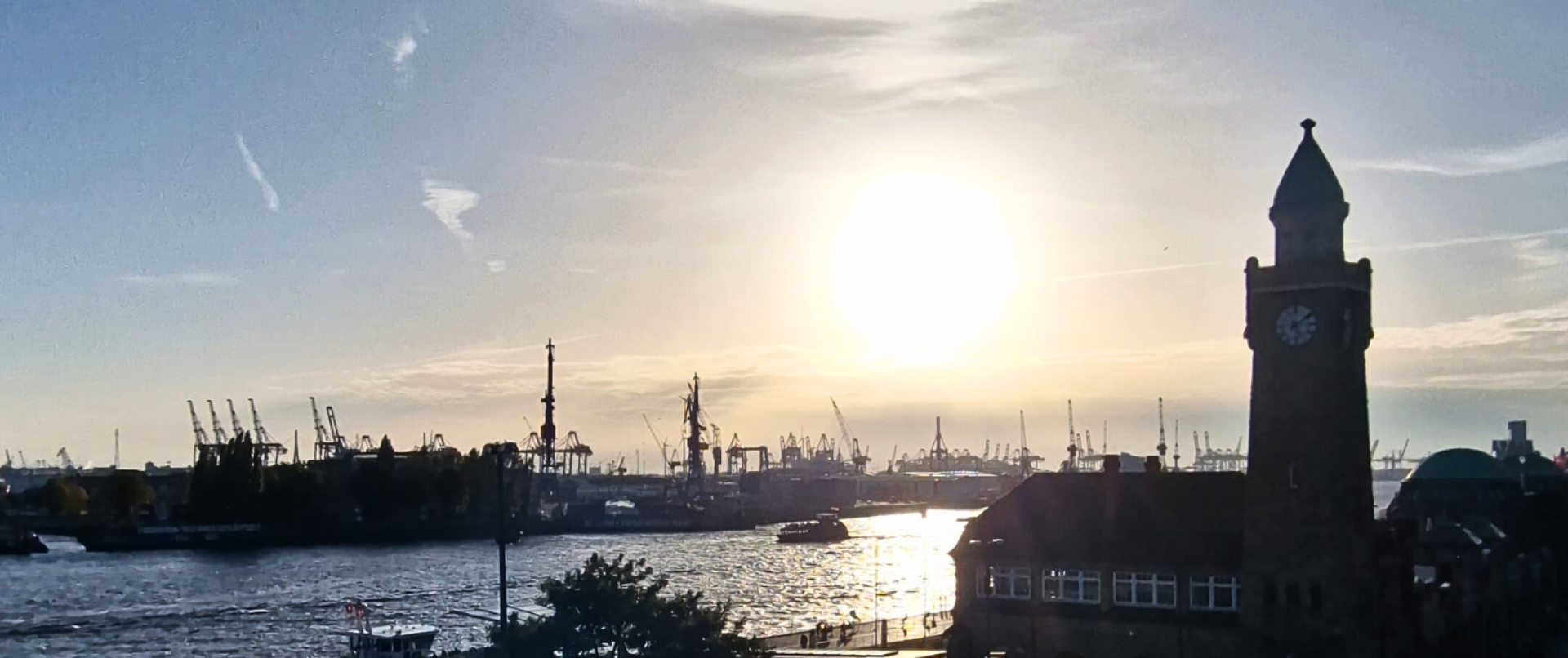 Sonnenuntergang über der Elbe mit Hafenkränen und dem Uhrturm der Hamburger Landungsbrücken.